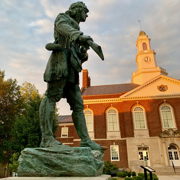 Bronze statue of a man with a gun in front of a historic building